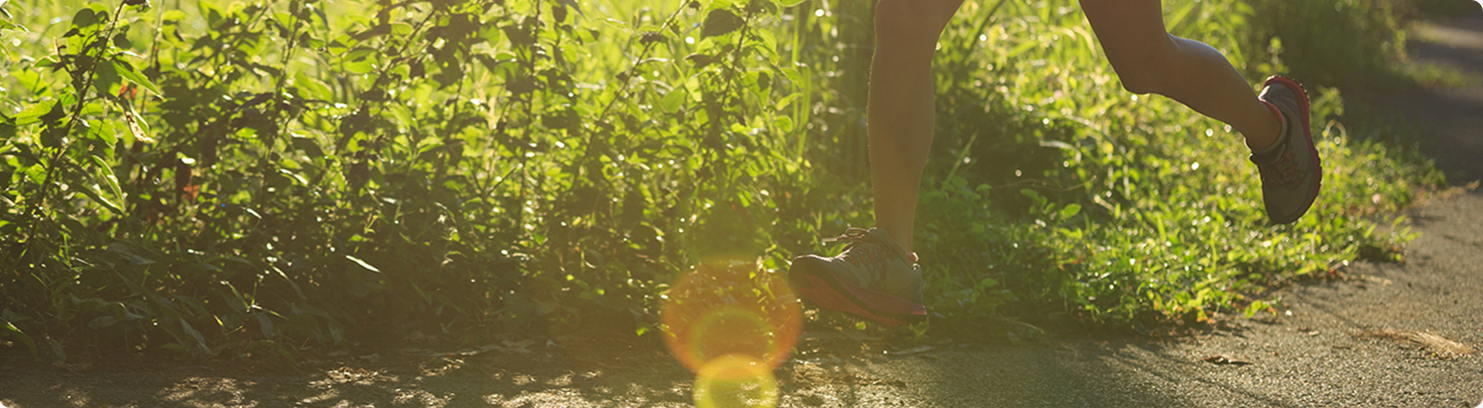 Person running on a sunlit path beside green plants, with visible legs in motion and sunlight creating lens flare across the scene—staying active can support wellness, just like the right medication for phlegm and cough.