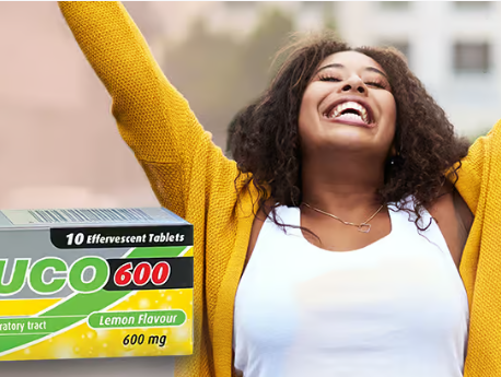A smiling woman with arms raised in joy, wearing a yellow sweater, stands outdoors. In the foreground, a box of MUCO 600 effervescent tablets—an otc mucolytic medication for phlegm and cough—is visible.