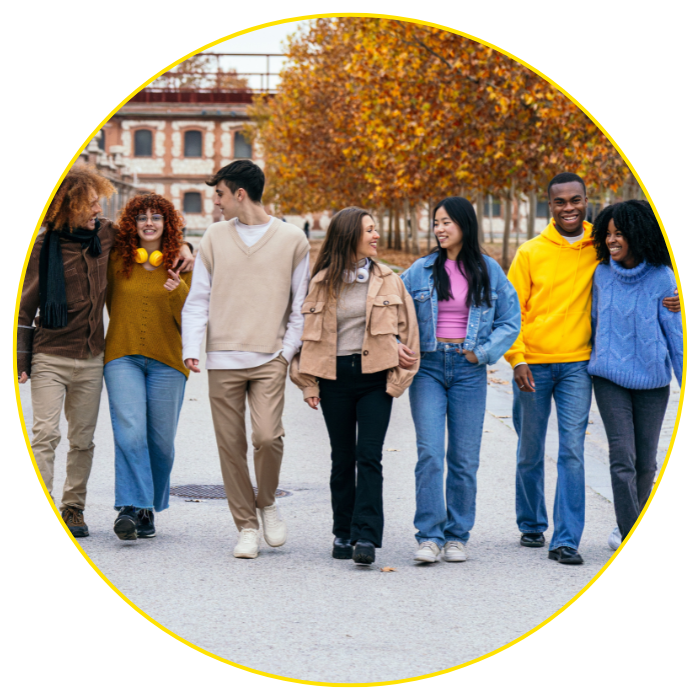 Six young adults walk outdoors together in autumn, smiling and talking. Dressed in casual fall clothes, they stroll among yellow-leaved trees, discussing the benefits of otc mucolytic medication for phlegm and cough.